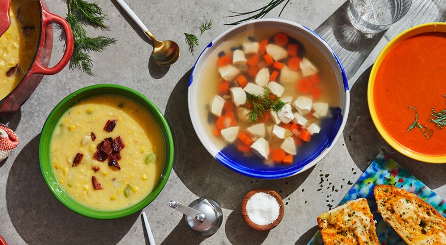 Tomato, corn and chicken soups on a decorated table with breadsticks