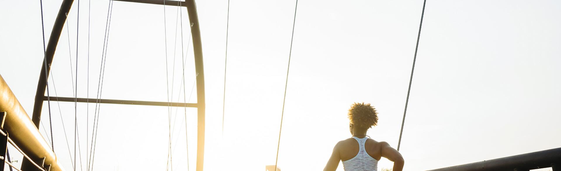 A photo of a woman running down a bridge at sunrise.