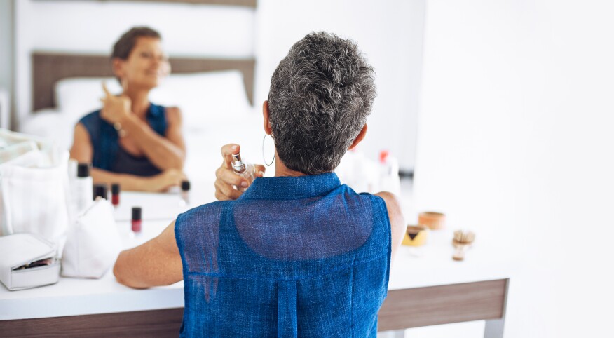 Middle aged woman applying perfume fragrance at her vanity mirror
