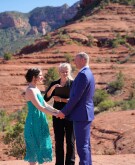 A couple with their officiator standing on red rocks for their private wedding ceremony
