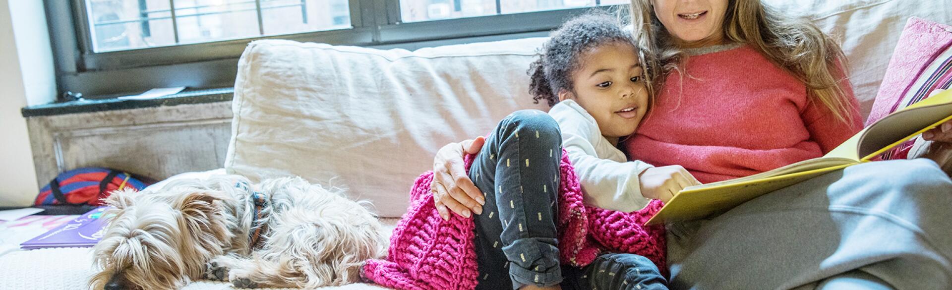 mom reading to her adopted daughter on a couch next to a dog