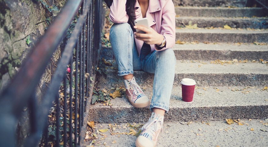 Unhappy young girl sitting at the steps outside and texting