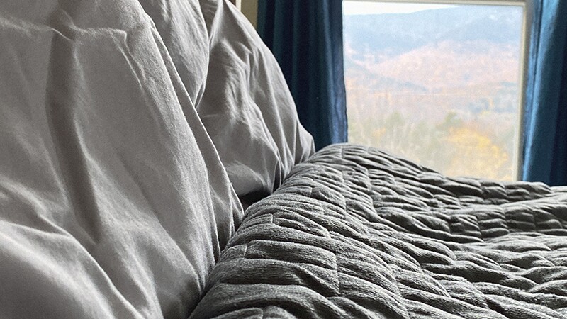 A weighted blanket on a bed with a window in the background