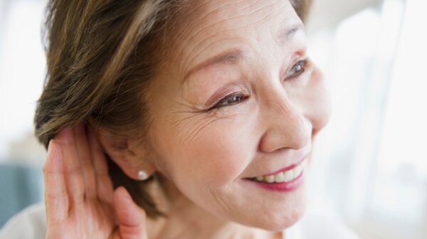 Una mujer acerca su mano a la oreja para escuchar mejor.