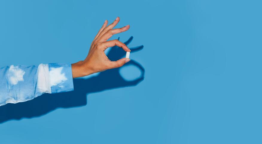 Hand holding out a vitamin on a blue background
