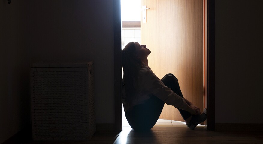 young teenager sitting on floor at end of long hallway appearing sad