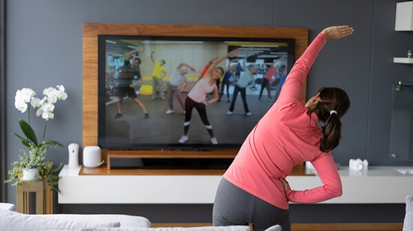 Back view of a woman stretching as she watches an exercise class on TV