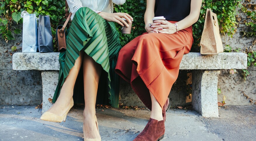 two women sitting on a bench drinking coffee together 