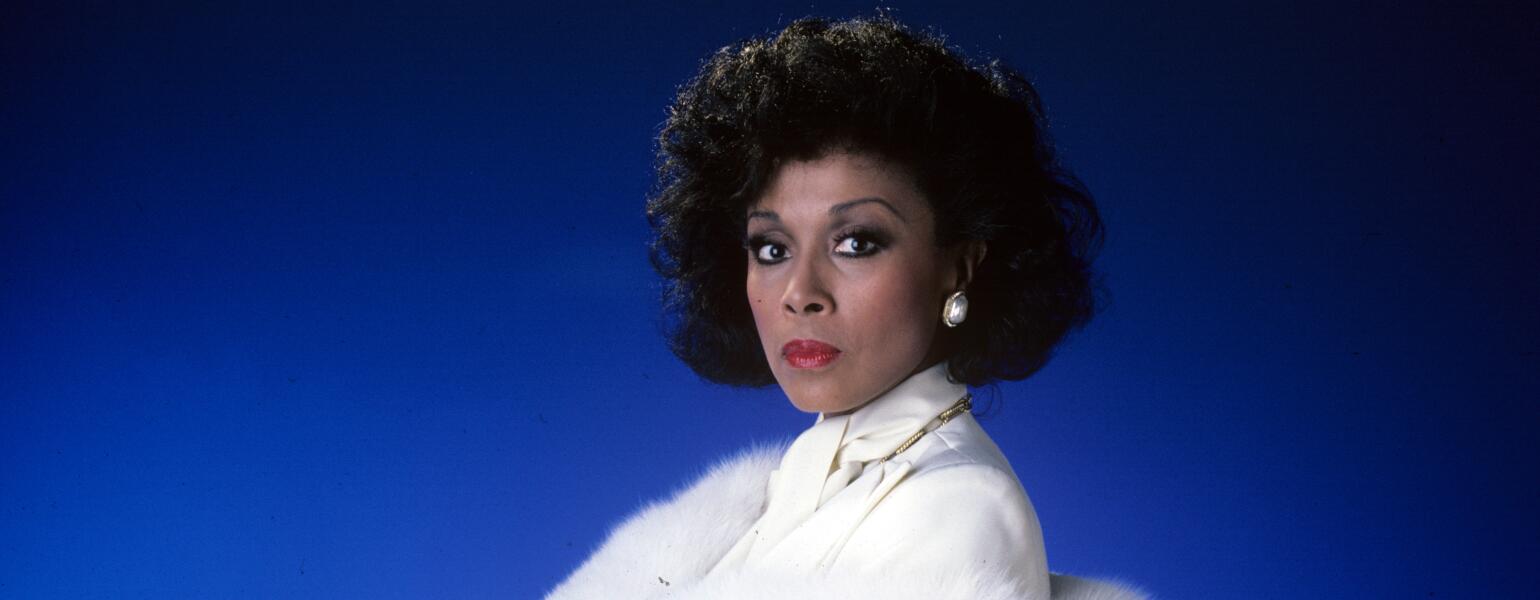 Diahann Carroll on blue background in white suit from TV show Dynasty