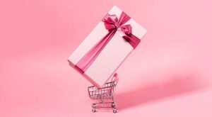 Shopping cart with giant pink gift with pink bow on pink background