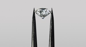 Diamond in tweezers on grey background