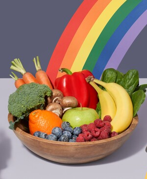 Woman with a rainbow bowl of fruits and veggies between two hands will flatware. 