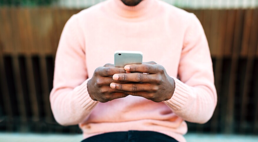 A man holds a cellphone, typing to an unknown person while sitting outside.