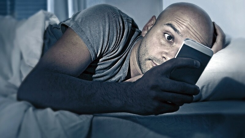 A man looking at his phone while in bed