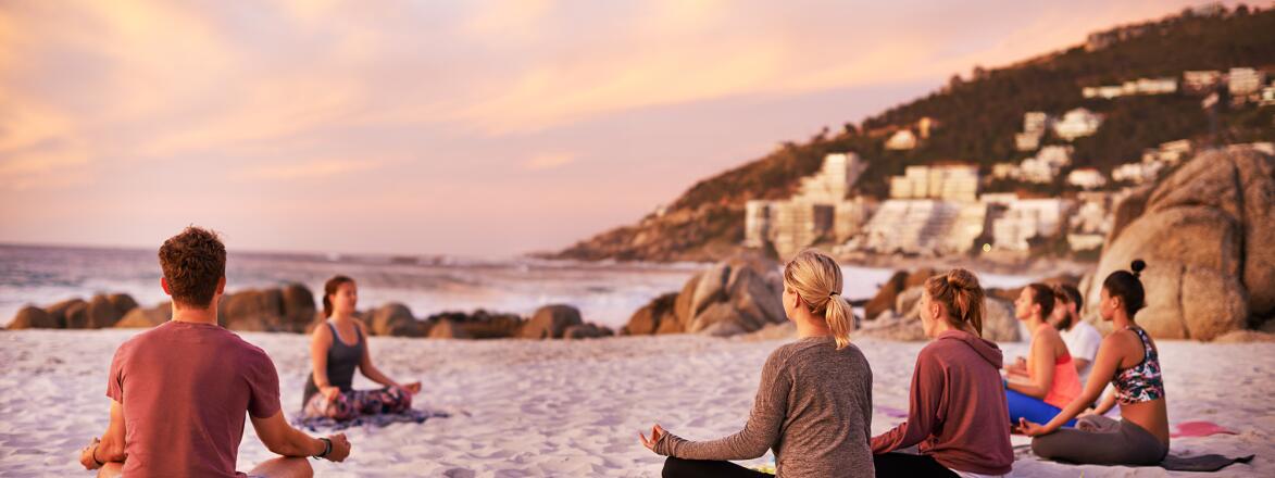 A handful of people doing yoga on the beach at sunset