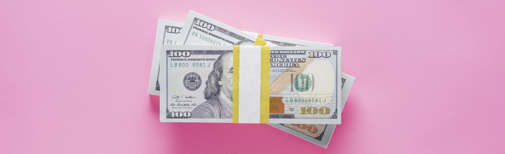 stacks of 100 dollar bills on pink background