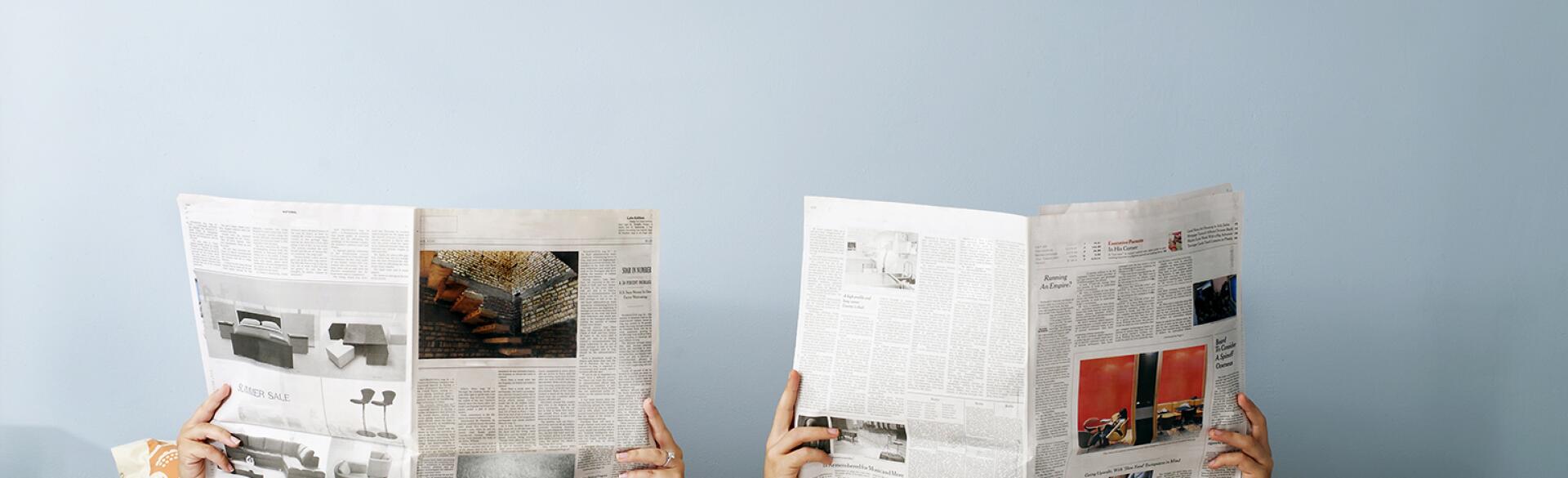 young couple laying in bed reading separate newspapers