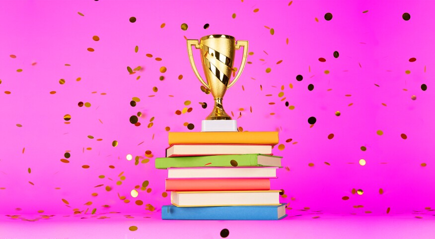 photo of trophy on stack of books against pink background and gold confetti