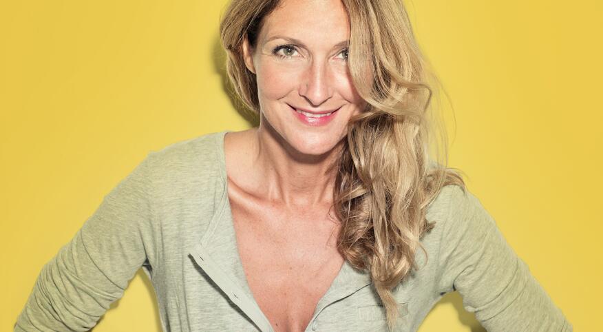 Portrait of confident blond woman in a pastel grey shirt in front of a yellow wall