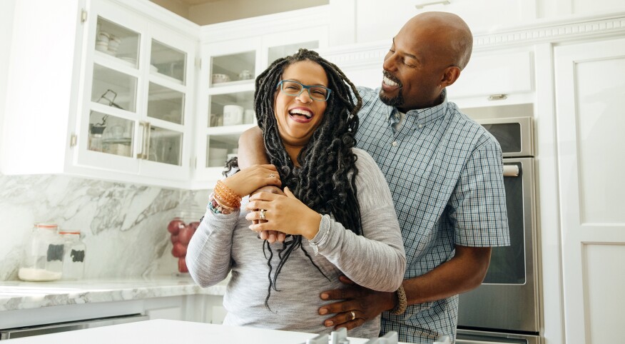 Smiling man embracing female partner in kitchen at home