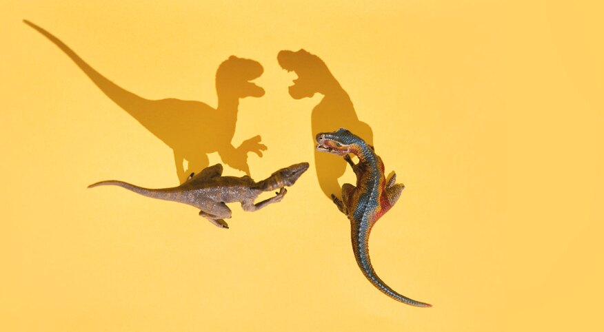 Two toy dinosaurs with mouths open casting long angry shadows