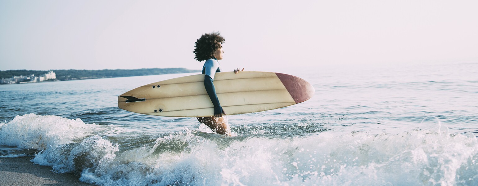 photo_of_african_american_woman_walking_in_ocean_with_surfboard_Surfing_GettyImages-1013089202_1540