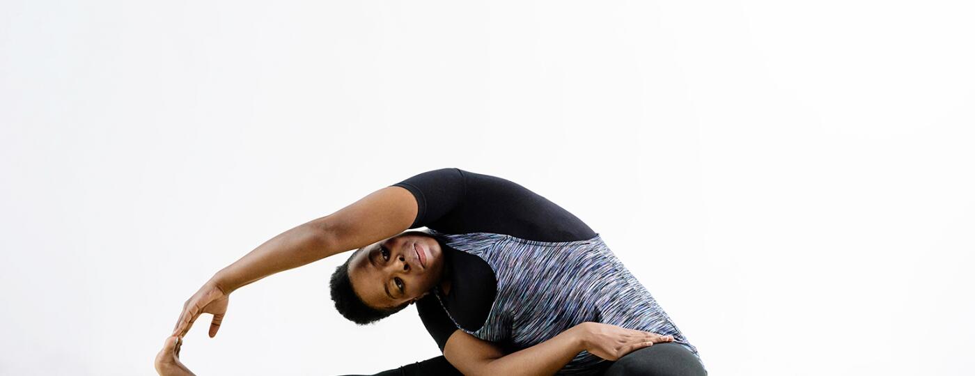A photo of woman bent to her right side in a yoga pose, while sitting on a yoga mat.