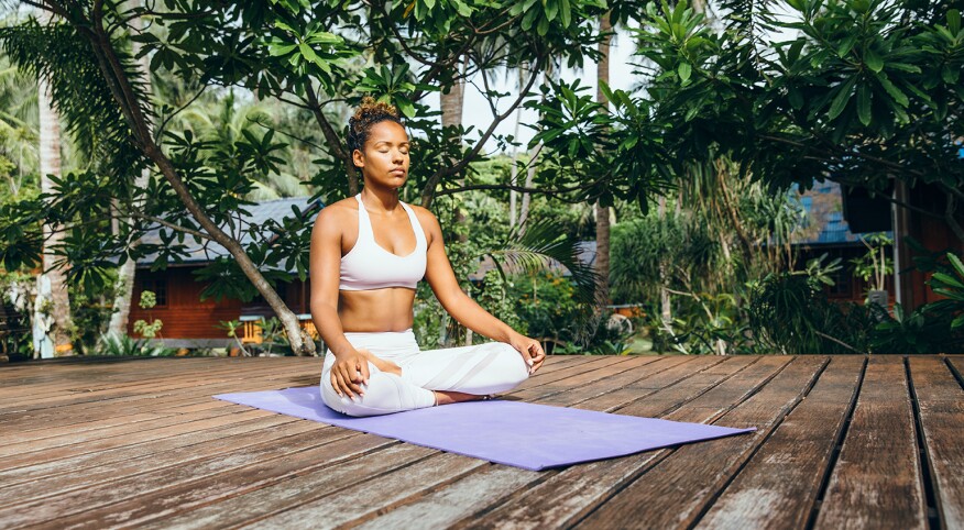 A photo of a woman sitting cross-legged on a yoga mat as she practices mindfulness and meditation.