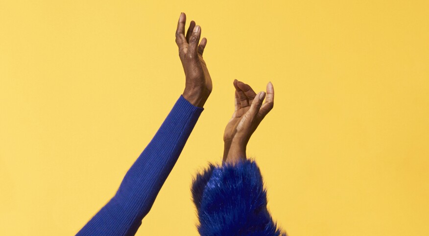 hands of two mature women dancing wearing blue long sleeve shirts on yellow background