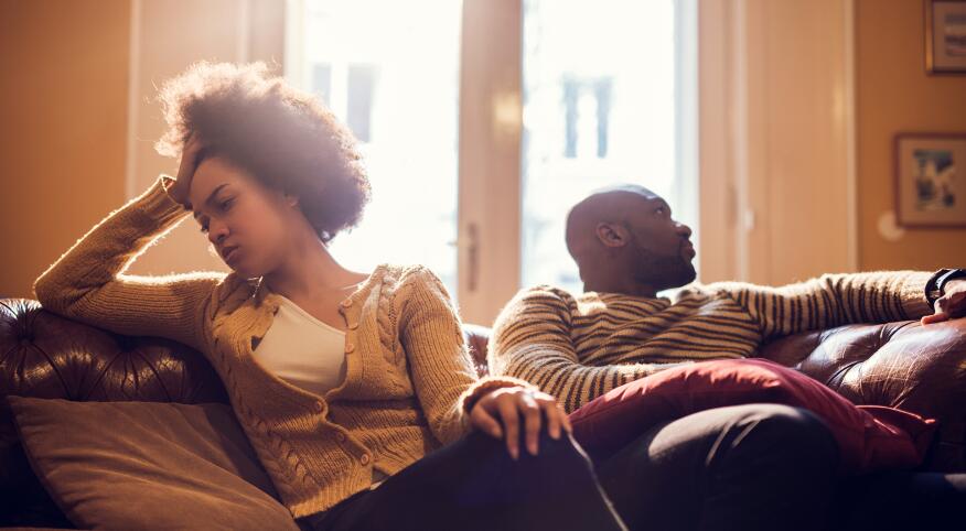 Black woman upset sitting on couch with husband after finding out he was cheating on her.