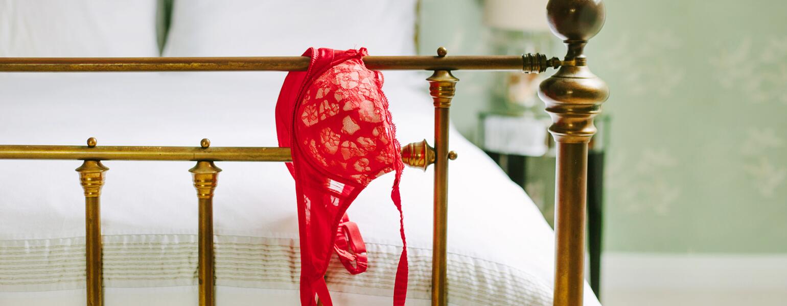end of bed post with red bra hanging off the edge