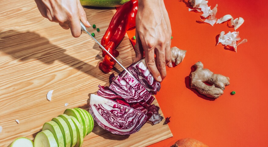 Woman's hand chopping vegetables on a cutting board with an orange background