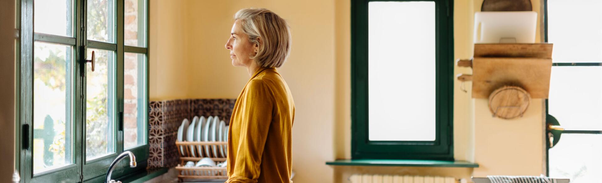 Woman standing in a kitchen at the sink looking out a window