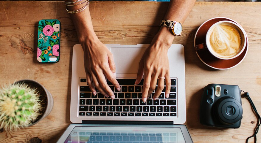 Woman Sitting At A Coffee Shop Working On A Laptop & Drinking A Latte.