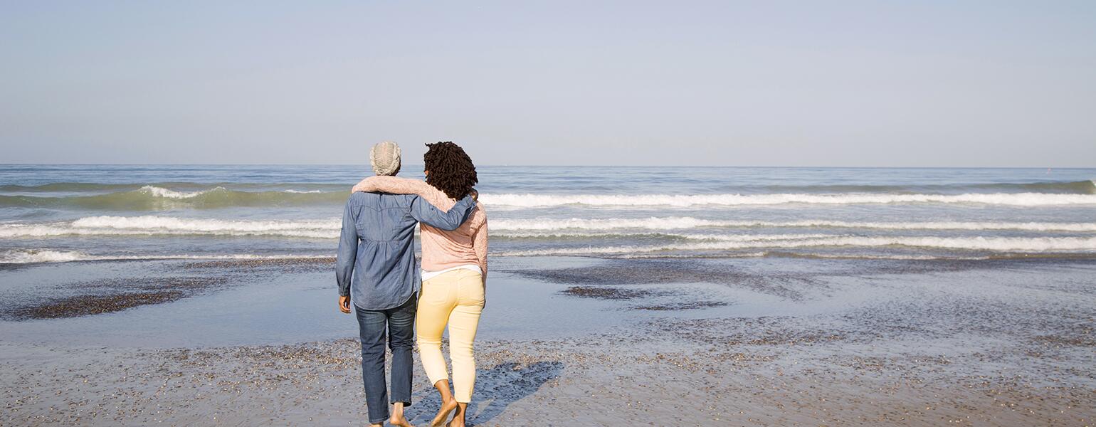 Black women hugging and walking on beach