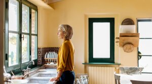 Woman standing in a kitchen at the sink looking out a window