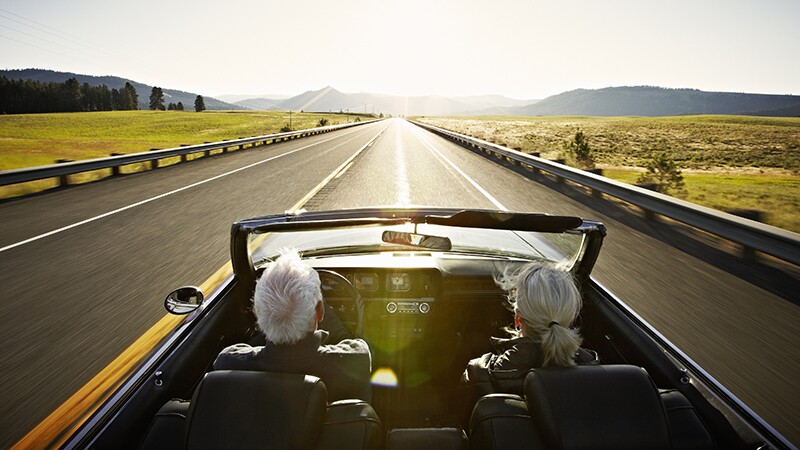 A man and woman driving in a convertible on an open road