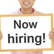 Now hiring sign on whiteboard held by smiling man