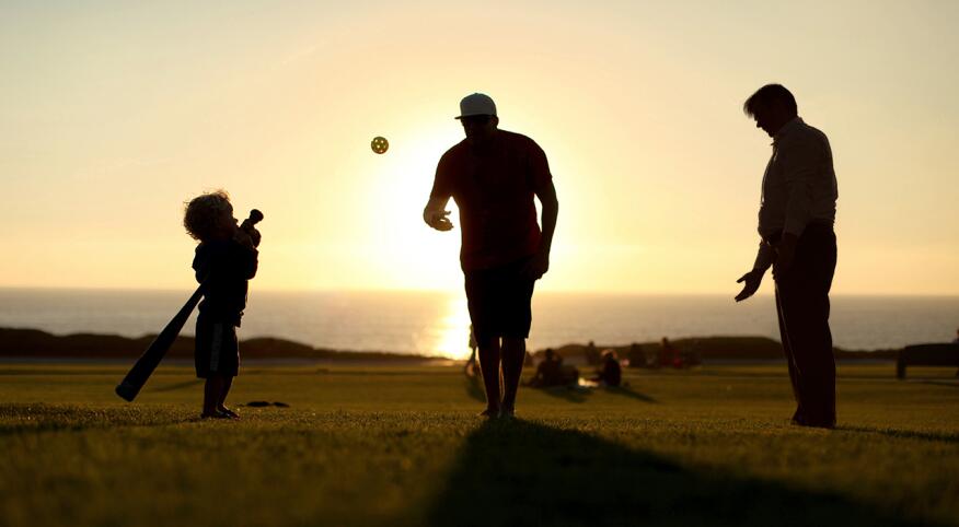 Two men playing baseball with young child at sunset