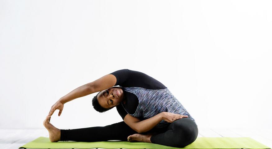 A photo of woman bent to her right side in a yoga pose, while sitting on a yoga mat.
