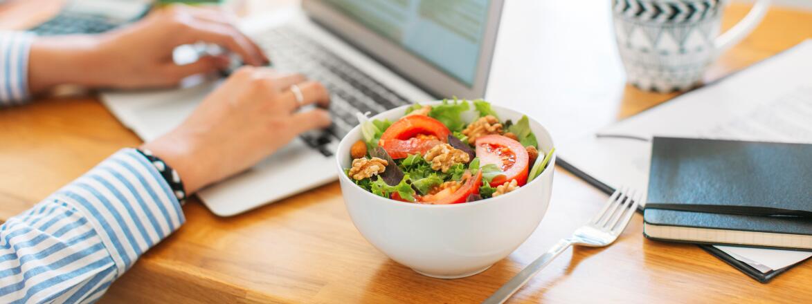 Woman typing on laptop eating a salad