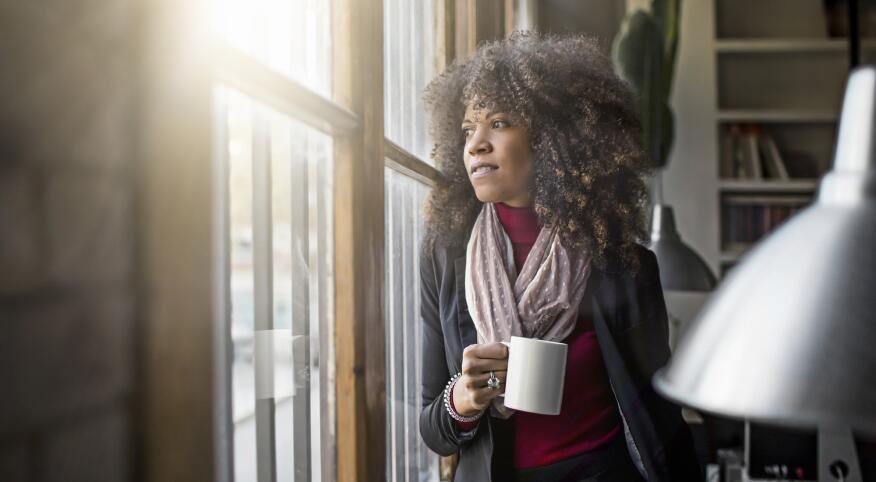woman holding a cup of coffee looking out her window