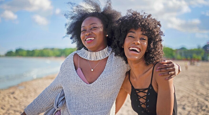 A photo of two best friends with their arms around each other on a beach.