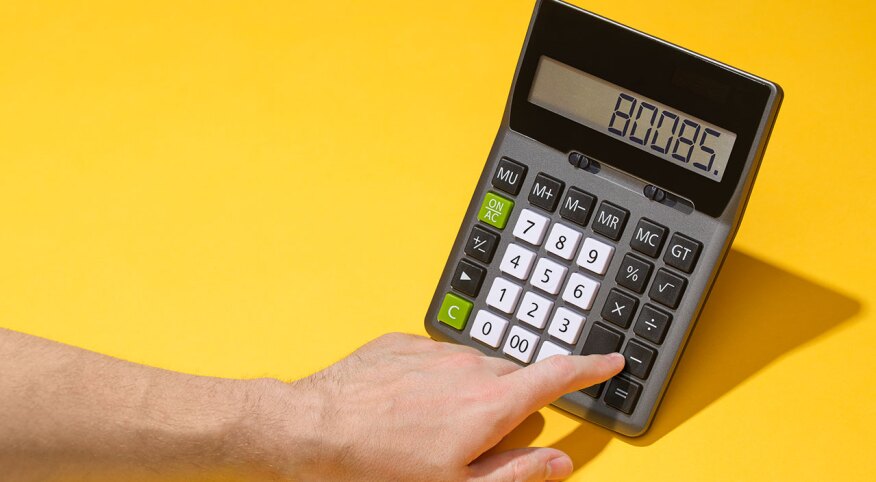 Hand typing numbers into calculator on yellow background