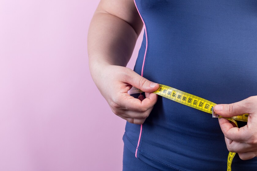 Overweight woman measuring her waist with measuring tape