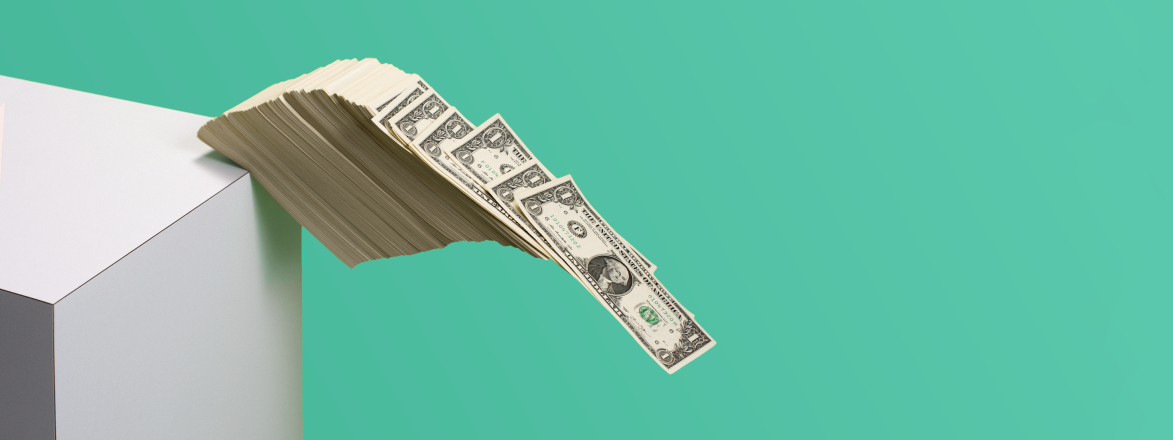 Stack of dollar bills falling of the edge of a shelf on a green background