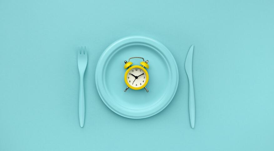 Intermittent fasting, lunch time. Yellow alarm clock, plate and cutlery. Blue background. Minimalistic concept