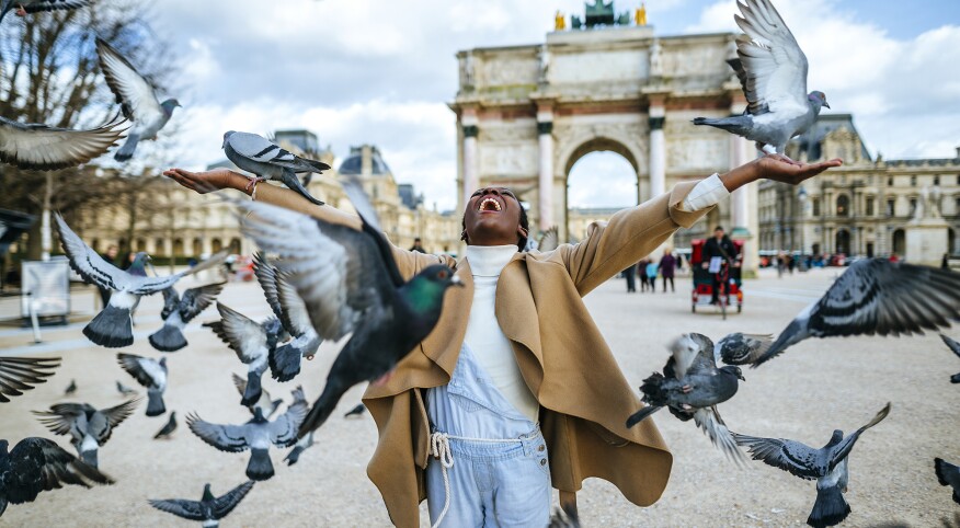 France, Paris, Happy young woman with flying pigeons at Arc de Triomphe