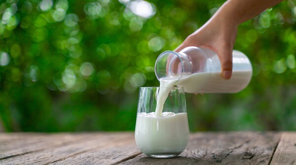 Milk being poured into a glass on a wooden table outside