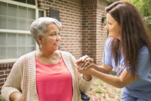 Wheelchair-bound African descent, female senior adult enjoys the outdoors with her home healthcare nurse or caregiver. The multi-ethnic group is at the patient's home or a nursing home or assisted living facility.
